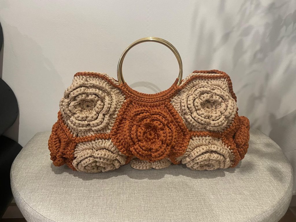 Sac à main "L'Éclosion d'Albi" en crochet, fait main par Vanda. Il présente des motifs floraux en rosettes terracotta et beige, avec une anse dorée. Création artisanale unique fabriquée en France.