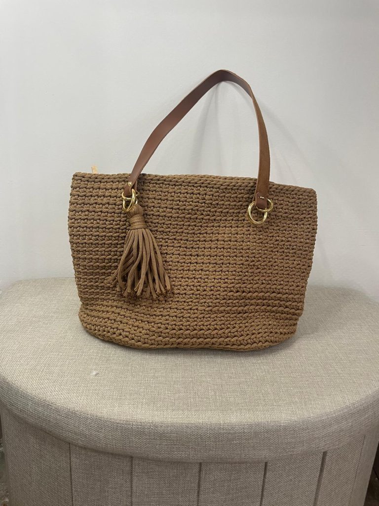 Sac à main en crochet de couleur camel beige, orné d'un gros pompon assorti sur le côté. Anse unique pour porté épaule avec anneaux métalliques dorés. Création artisanale française Vanda, style bohème chic.