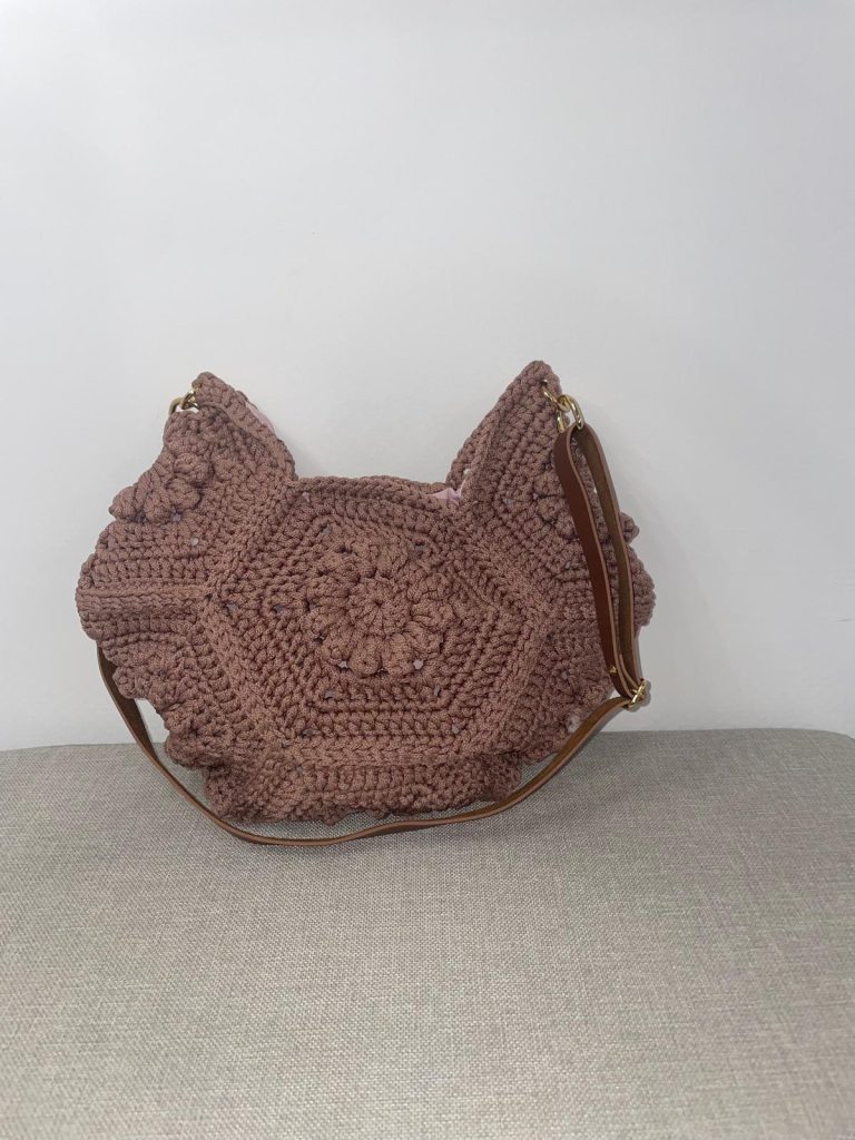 Sac à main en crochet couleur vieux rose, formé par l'assemblage de motifs hexagonaux avec un cœur en forme de fleur en relief. Fine bandoulière marron attachée par des anneaux dorés. Création artisanale romantique Vanda.