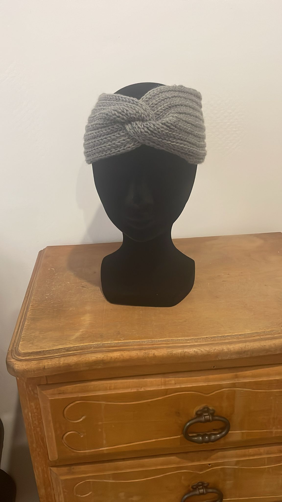Bandeau d'hiver pour femme en crochet gris souris avec torsade sur le devant (style turban). Accessoire cheveux chaud et mode présenté sur une tête de mannequin noir. Création artisanale fait main par Vanda Albi