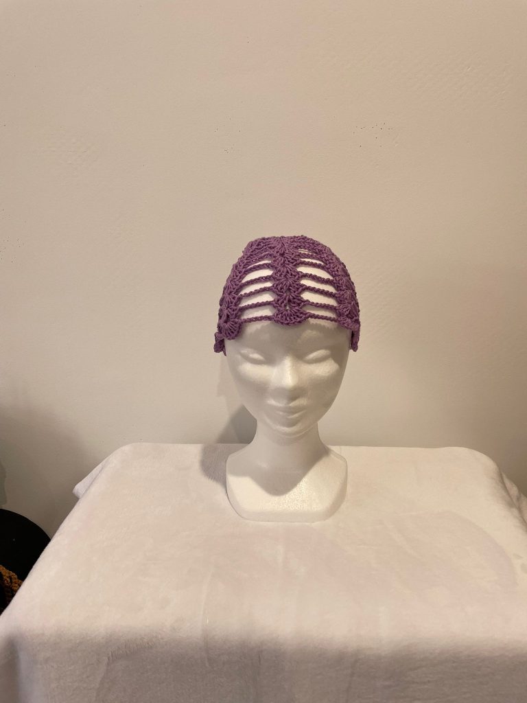 Accessoire de tête type bandeau large ou coiffe en crochet de couleur mauve lilas. Le motif est très ajouré, formant une résille délicate sur le dessus de la tête. Présenté sur un mannequin blanc. Création artisanale bohème Vanda.