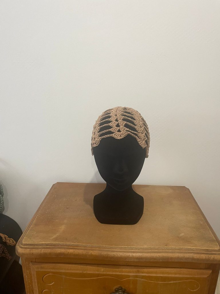 Bonnet court type calot en crochet couleur beige sable / nude. Motif ajouré géométrique style rétro années 20, présenté sur buste noir. Accessoire de tête élégant pour femme, fait main par Vanda Albi.