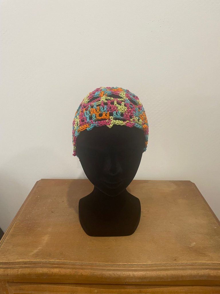Bonnet court d'été type calot pour femme en crochet multicolore (rose, orange, bleu, vert). Accessoire de tête style bohème chic présenté sur un buste noir. Création artisanale fait main par Vanda Albi.