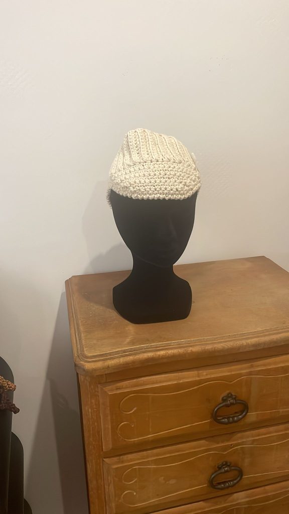 Casquette à visière pour femme en crochet couleur écru crème. Accessoire de mode style sportswear chic et tendance, présenté sur une tête de mannequin noir. Création artisanale fait main par Vanda Albi.
