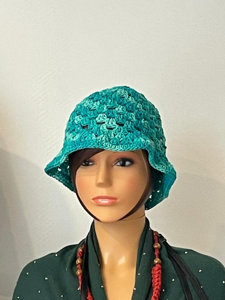 Chapeau type Bob (Bucket Hat) pour femme en crochet fait main. Couleur bleu turquoise et lagon nuancé avec motif point fantaisie. Présenté sur une tête de mannequin. Accessoire mode été artisanal Vanda Albi.
