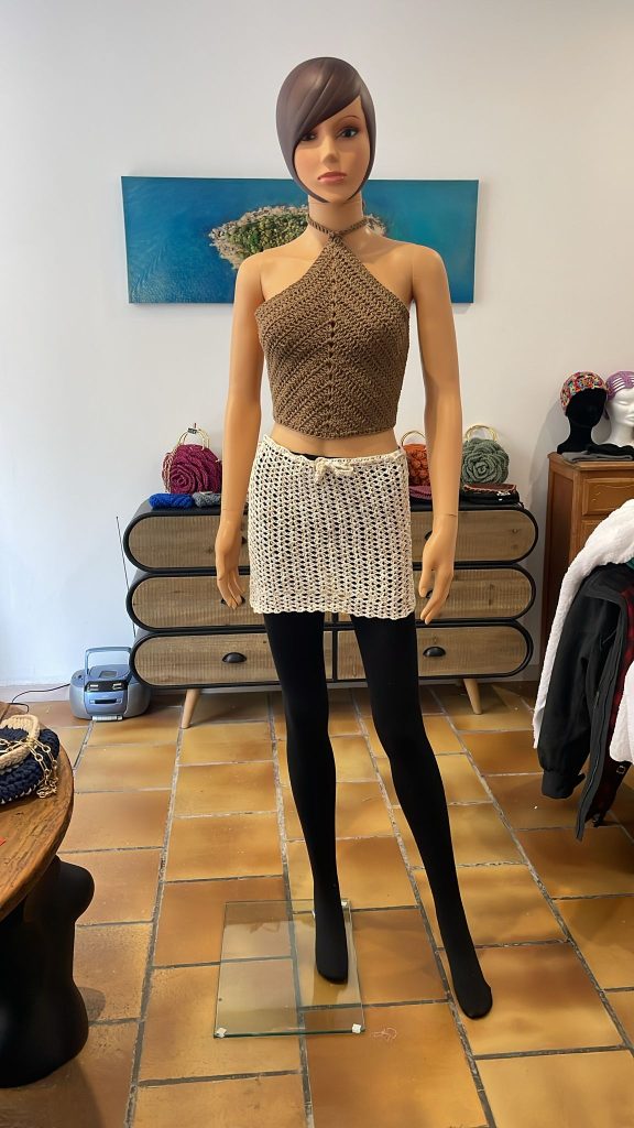 Ensemble d'été pour femme en crochet fait main. Composé d'un crop top dos nu couleur bronze à motif chevron et d'une mini-jupe en maille filet couleur crème. Tenue style bohème chic présentée sur mannequin. Création artisanale Vanda Albi.