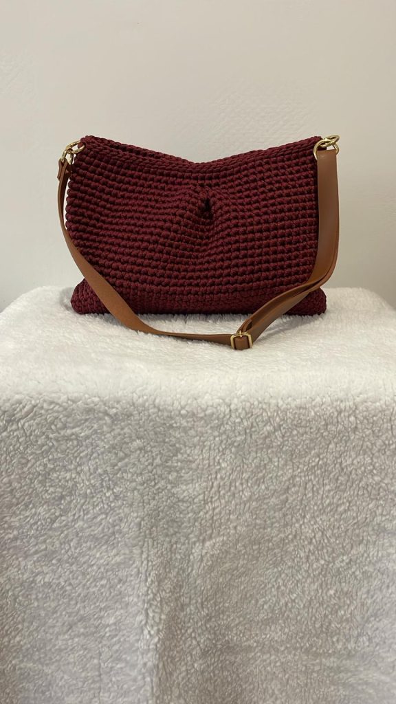 Sac à main rectangulaire en crochet de couleur bordeaux intense. Maille serrée avec un léger pli central esthétique. Bandoulière marron style cuir attachée par des anneaux dorés. Création artisanale française Vanda.