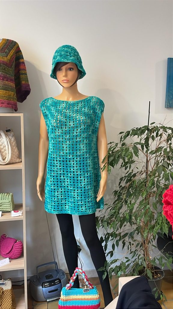 Tunique sans manches pour femme en crochet, couleur bleu turquoise et lagon nuancé. Point de maille aéré type filet, col bateau. Vêtement d'été artisanal présenté sur cintre et sur mannequin. Création Vanda Albi.